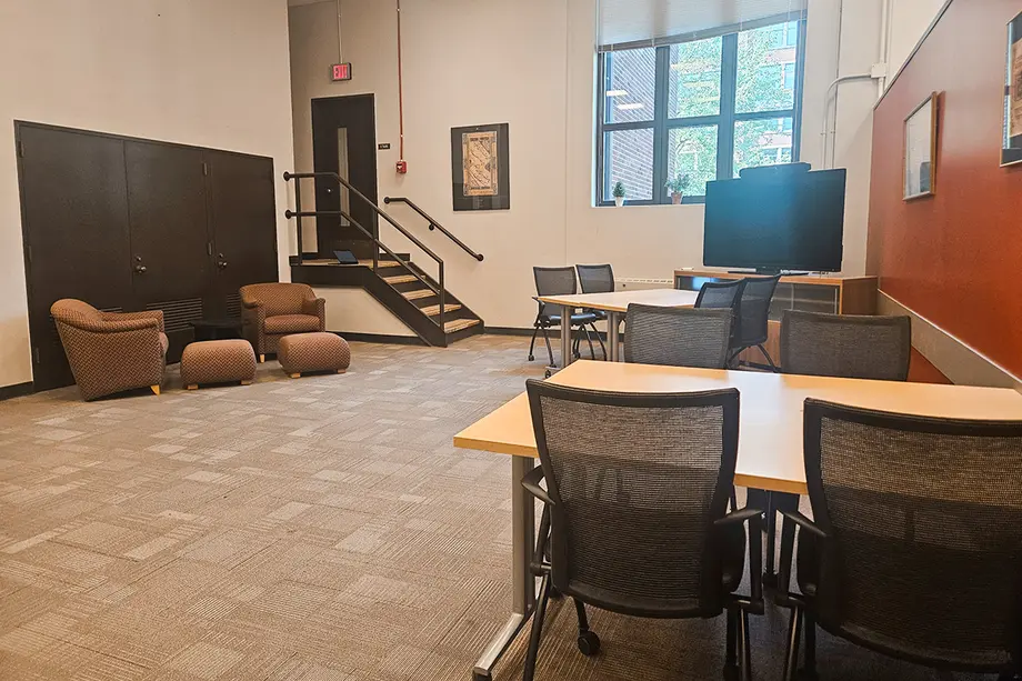 Open room with high ceilings, large pane windows, and tables with movable chairs.